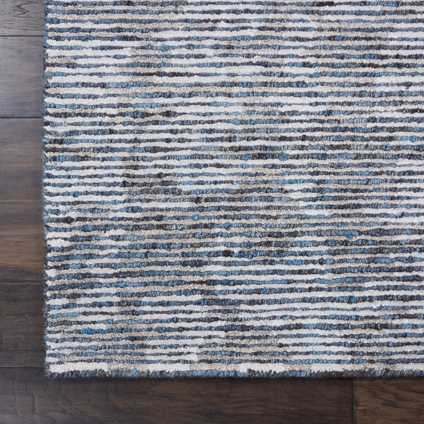 Blue and cream striped rug with textured pile on dark wood floor.