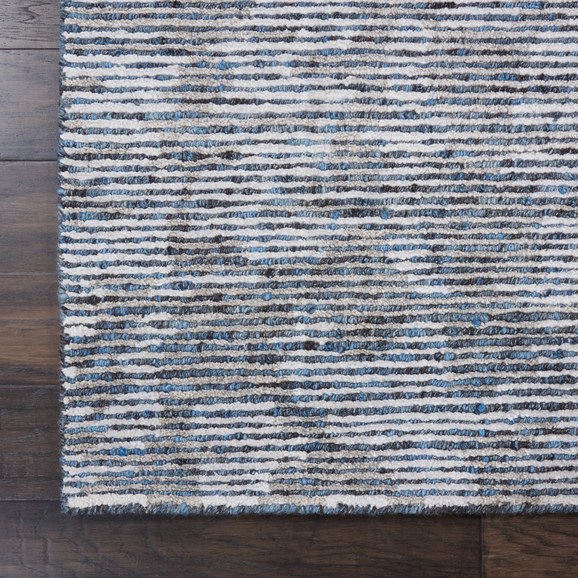 Blue and cream striped rug with textured pile on dark wood floor.