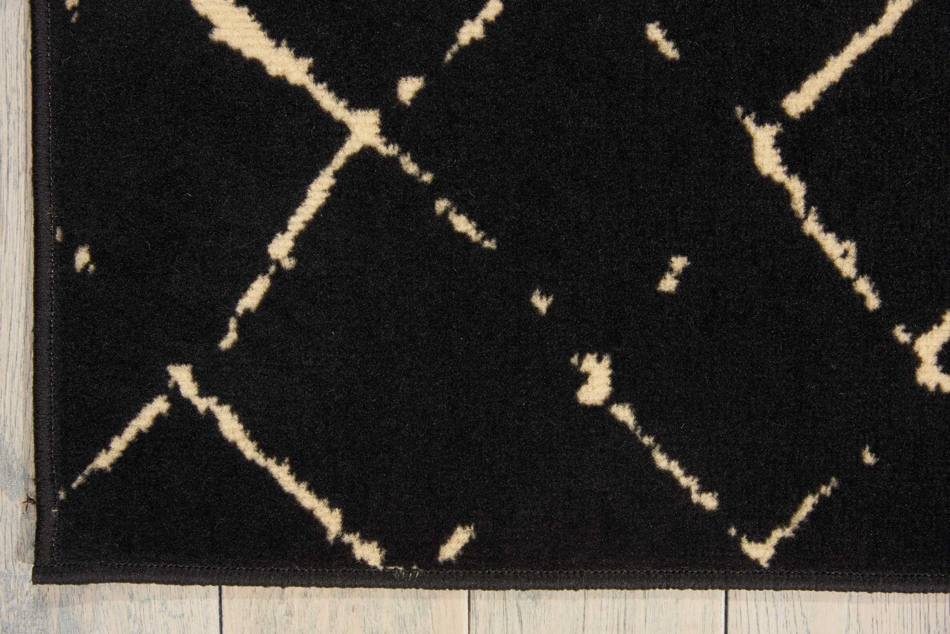Black plush rug with cream geometric lattice/diamond trellis pattern on wooden floor.