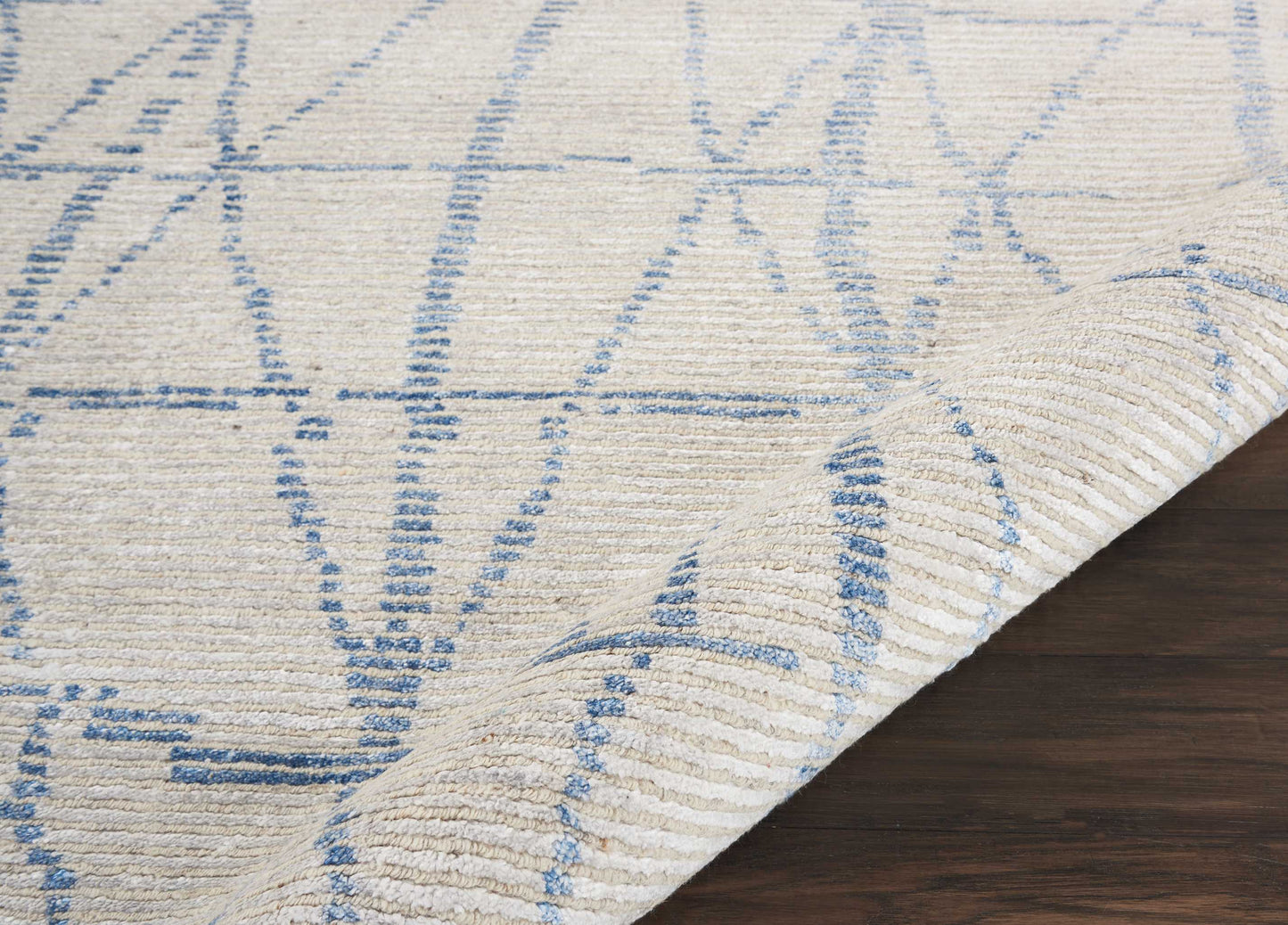 Cream rug with blue geometric line pattern, woven texture, folded corner on dark wood floor.