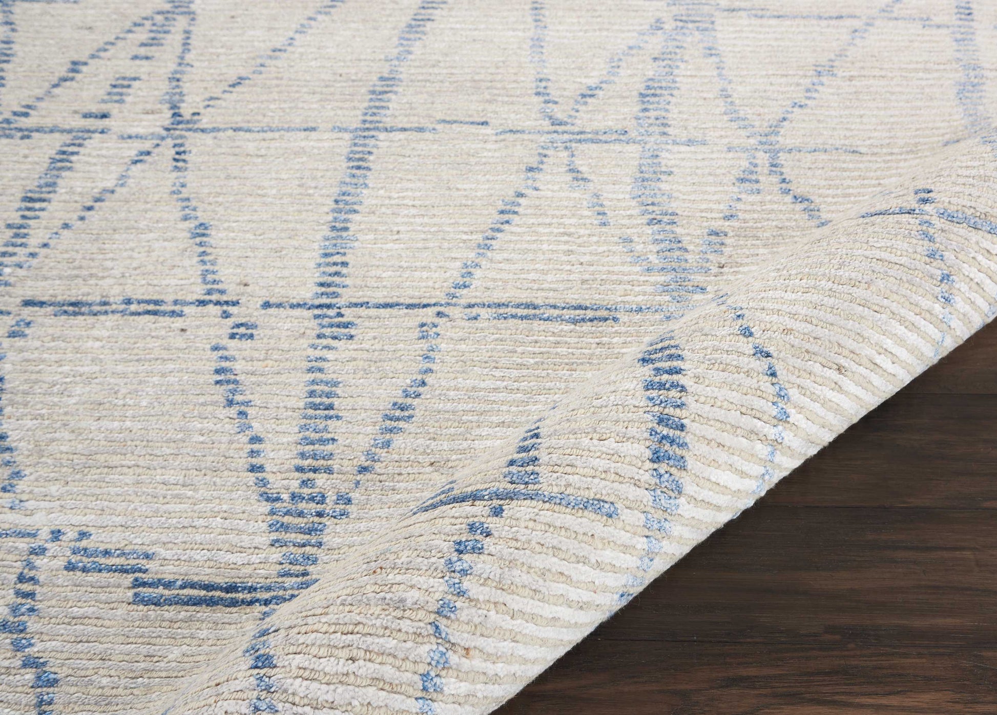 Cream rug with blue geometric line pattern, woven texture, folded corner on dark wood floor.