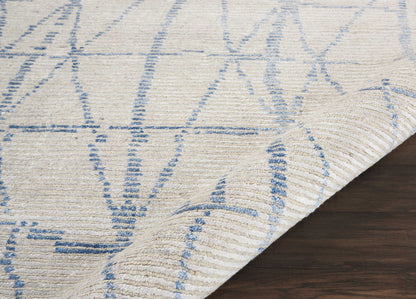 Cream rug with blue geometric line pattern, woven texture, folded corner on dark wood floor.