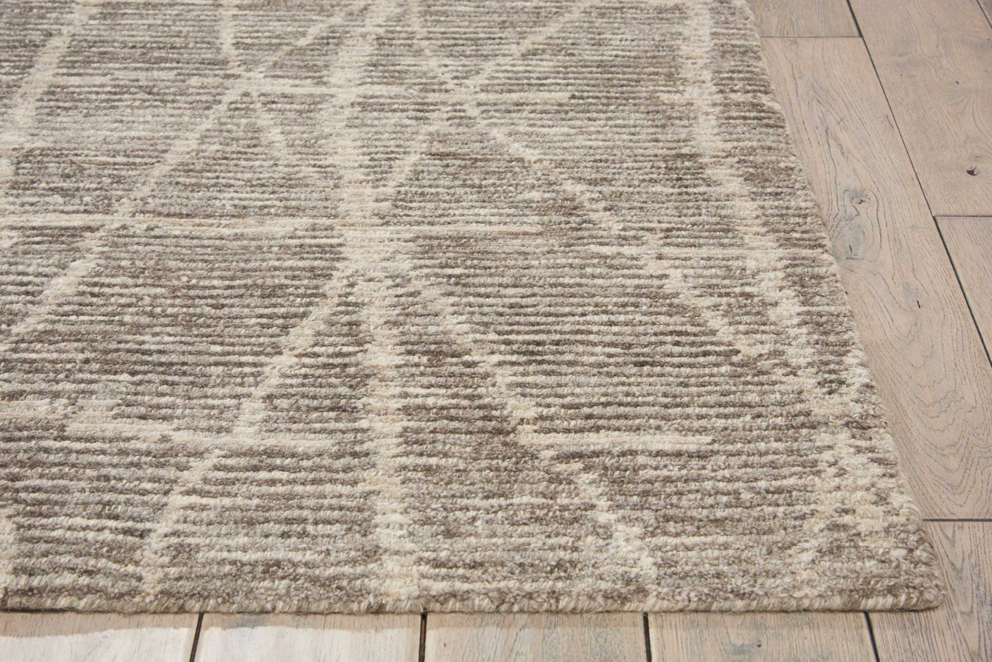 Textured beige and ivory geometric area rug with triangle line pattern on light wood floor.