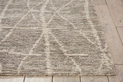 Textured beige and ivory geometric area rug with triangle line pattern on light wood floor.