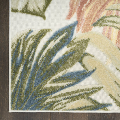 Close-up of a leafy rug corner featuring blue, green and beige leaves on white, with bound edge on dark wood floor.