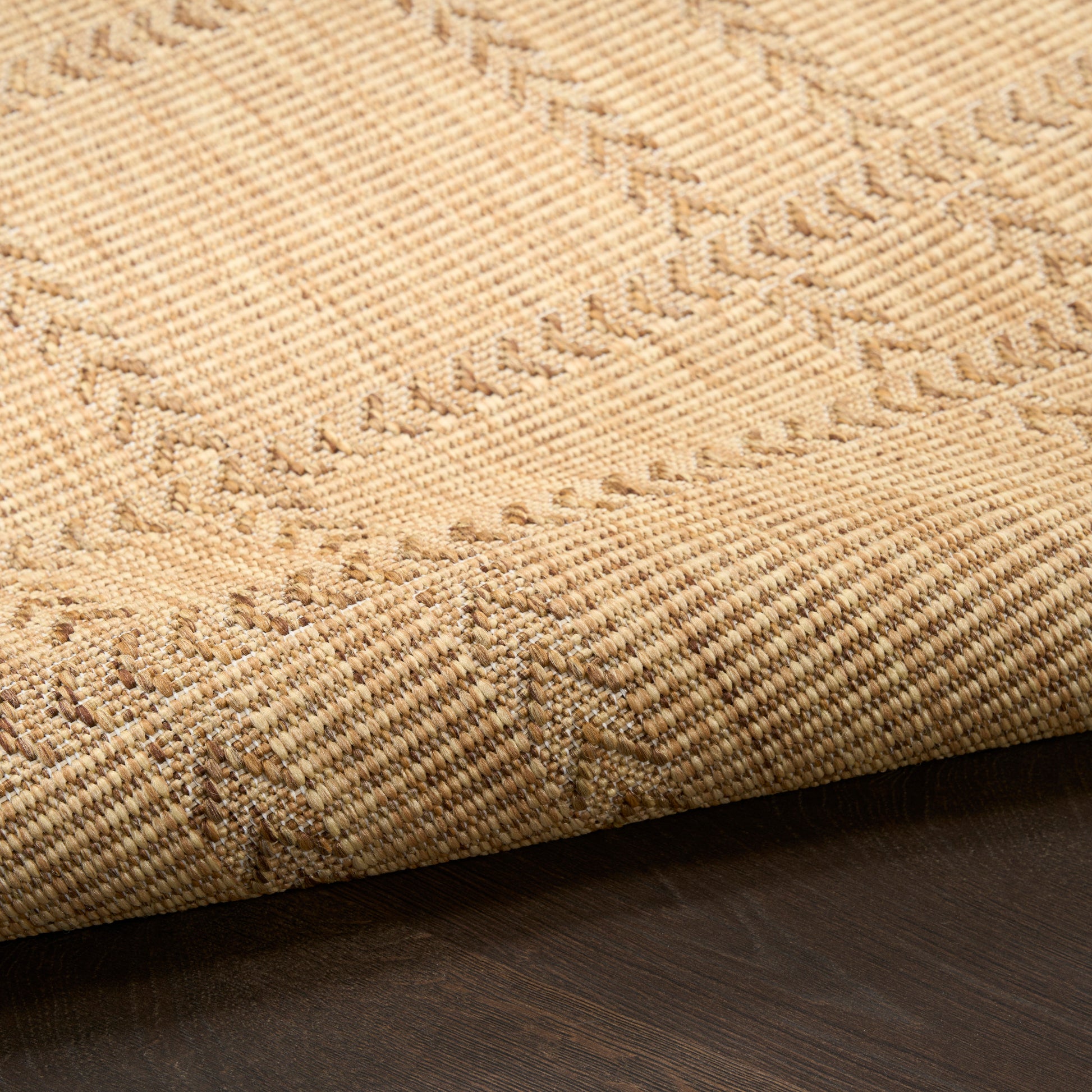 Natural beige jute rug with subtle geometric chevron pattern, folded edge on dark wood floor.