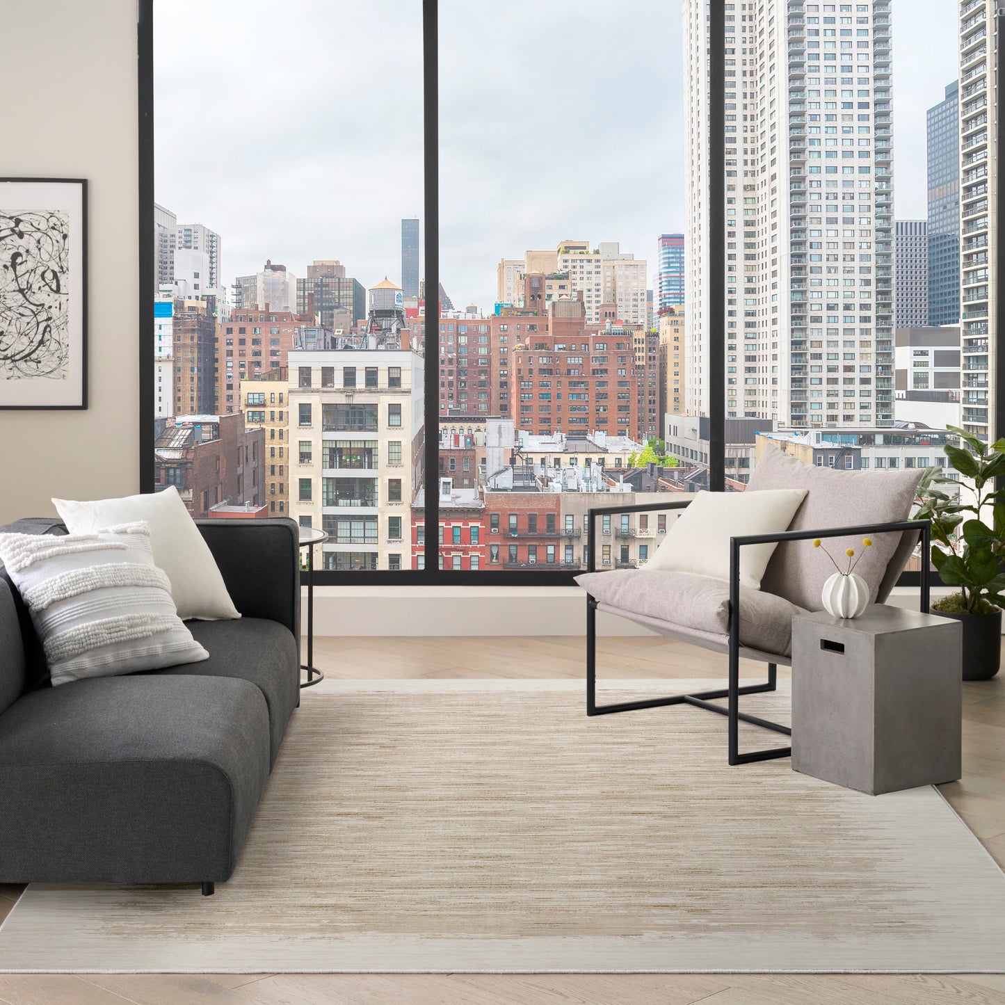Modern living room with city skyline windows, dark gray sofa, light gray metal-framed chair, beige rug, gray cube side table.
