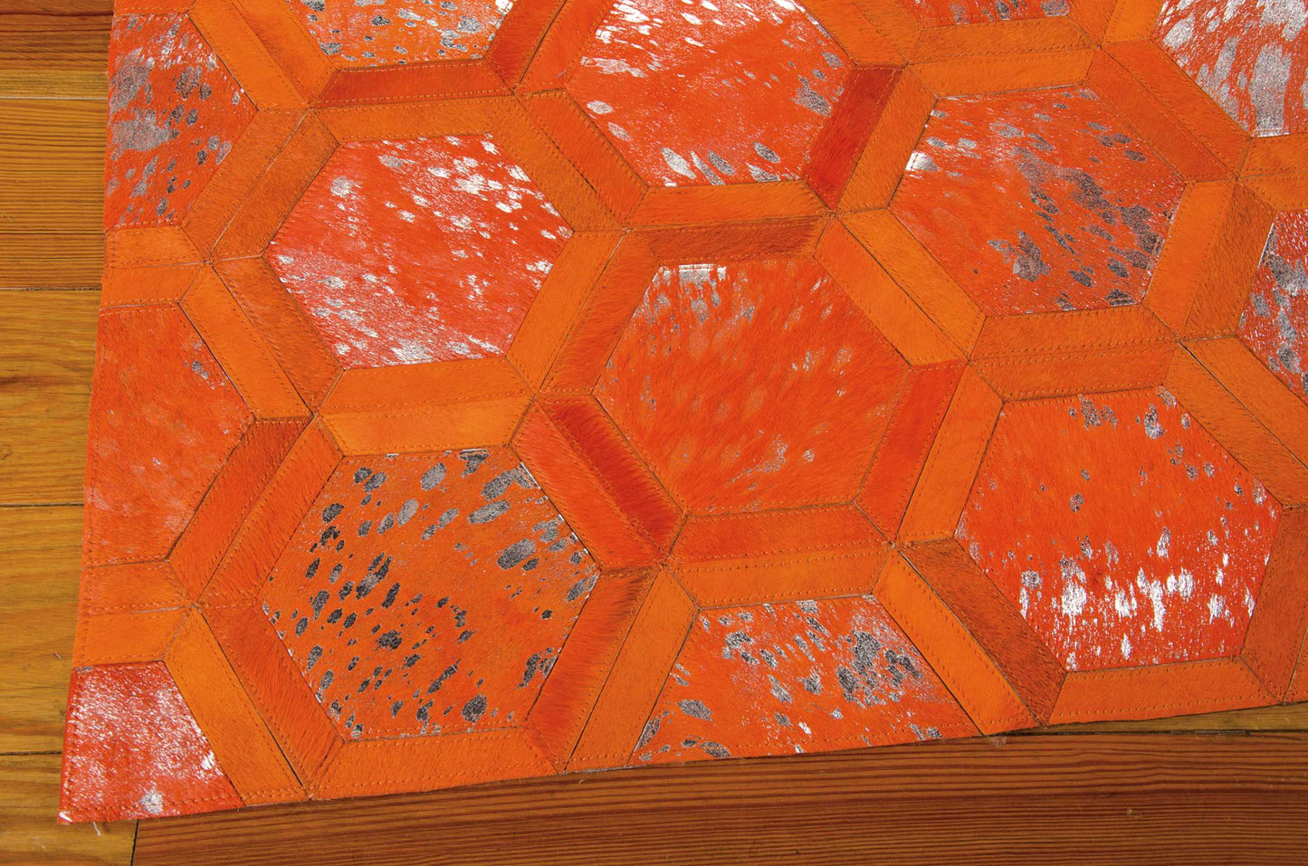 Orange hexagon patchwork rug with stitched borders and distressed speckled panels on a wooden floor.
