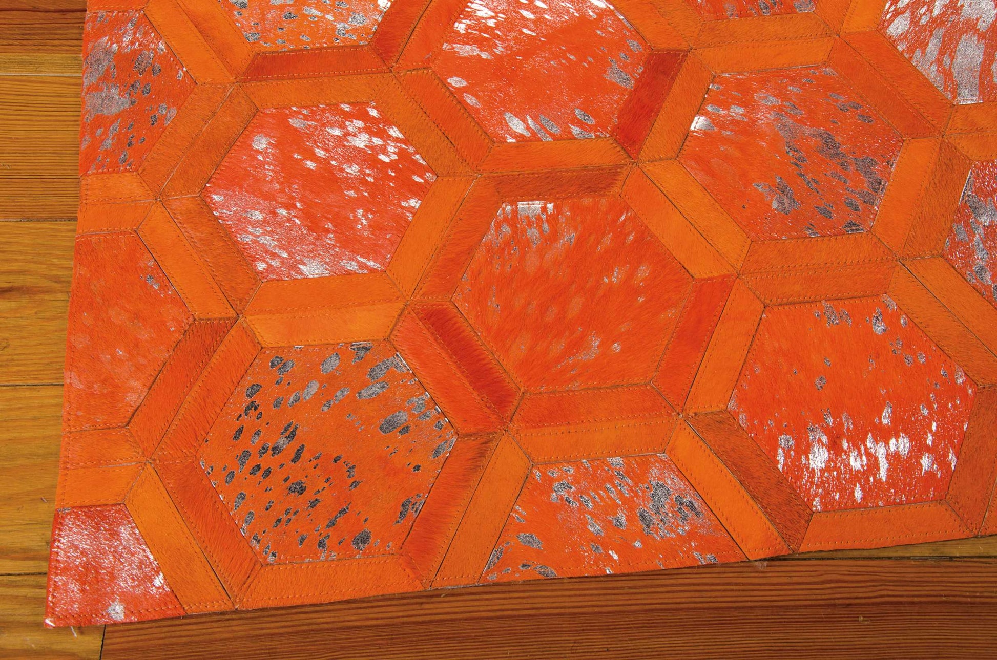 Orange hexagon patchwork rug with stitched borders and distressed speckled panels on a wooden floor.