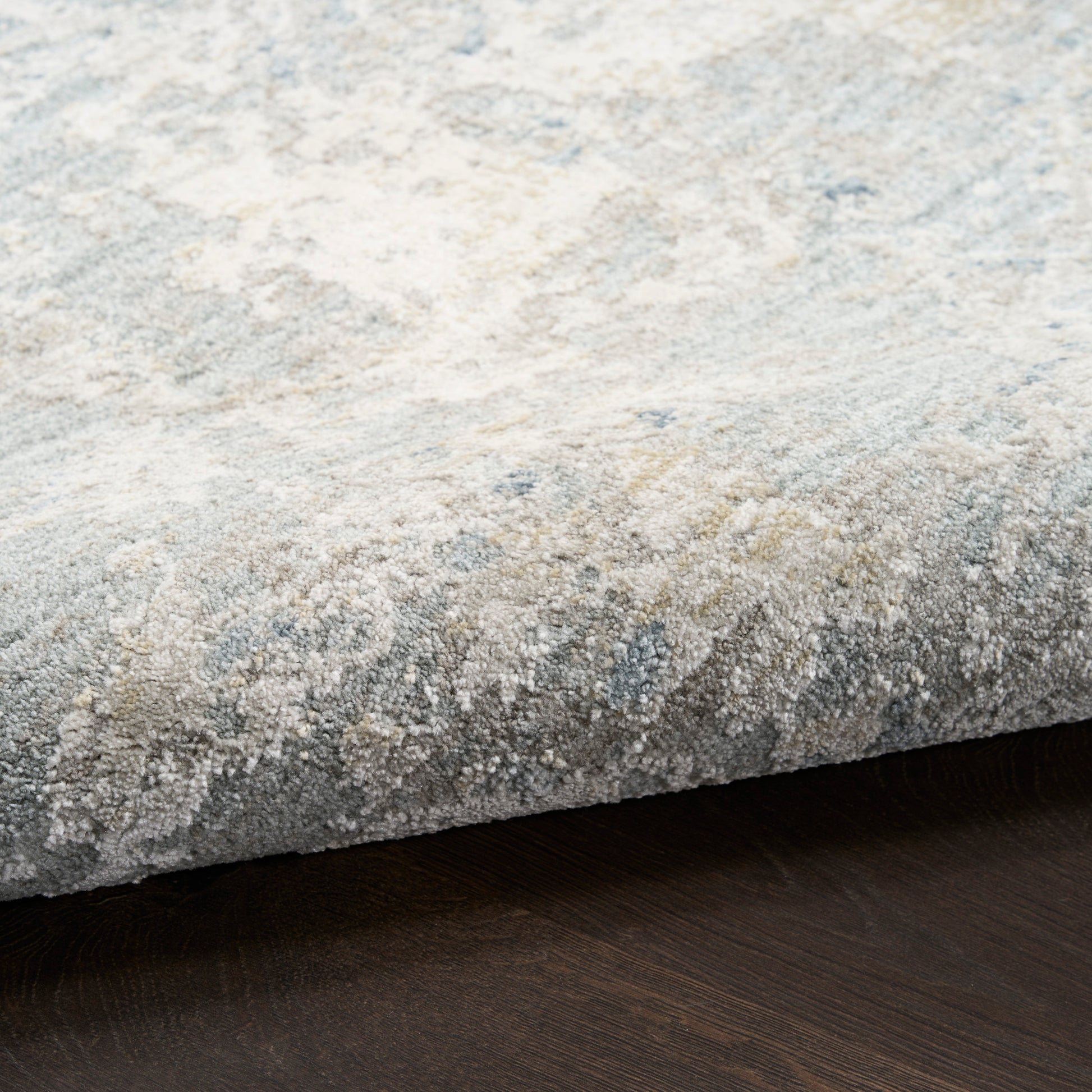 Close-up of a textured light gray and beige patterned rug edge on a dark wood floor.