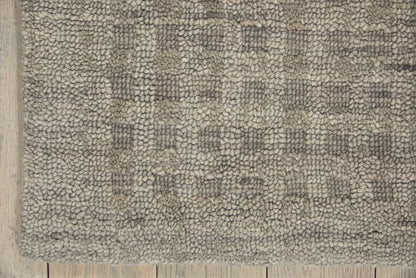 Gray-beige textured rug with dense loop pile, edge on light wood floor.