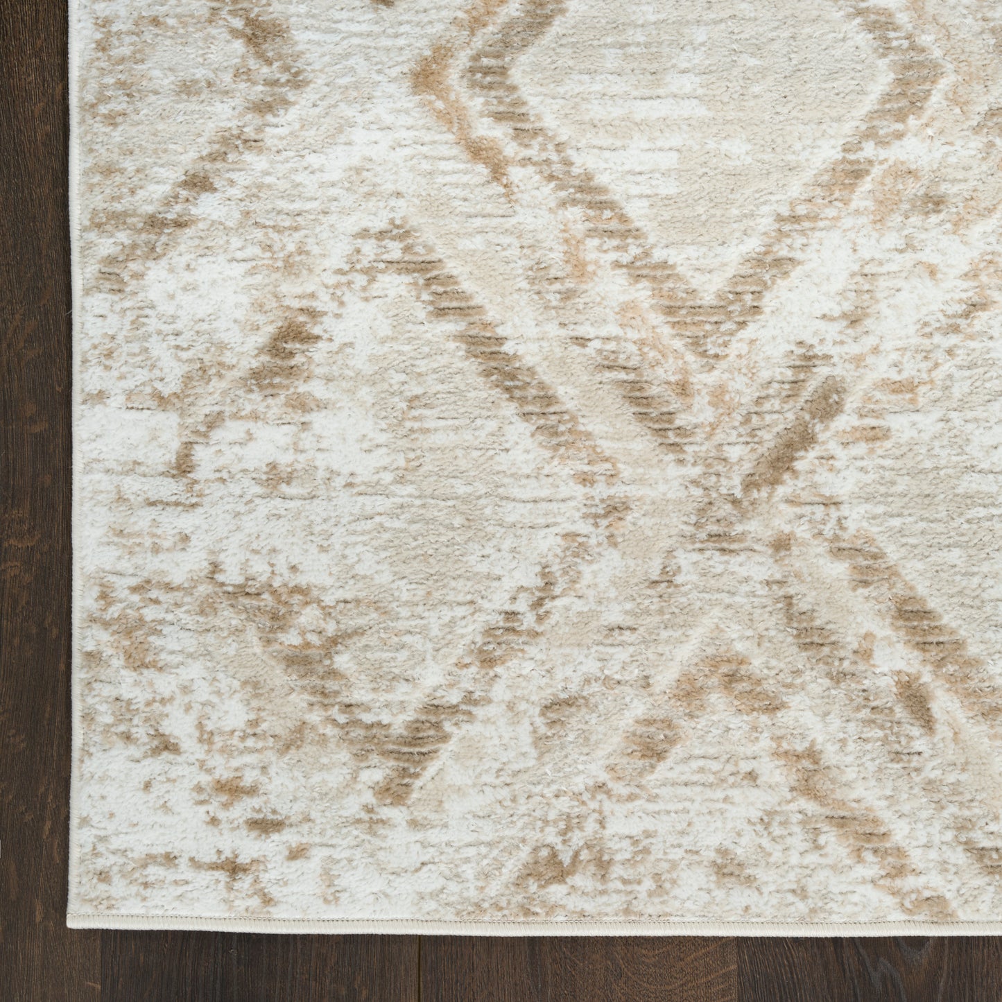 Beige plush area rug with tan diamond geometric pattern, distressed look, laid on dark hardwood floor.