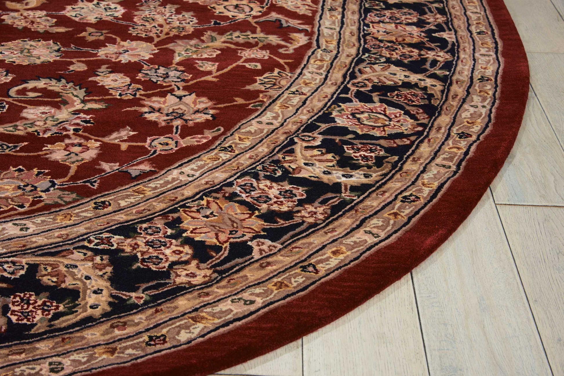 Round oriental rug with red field and intricate black and beige floral borders on a light wood floor.