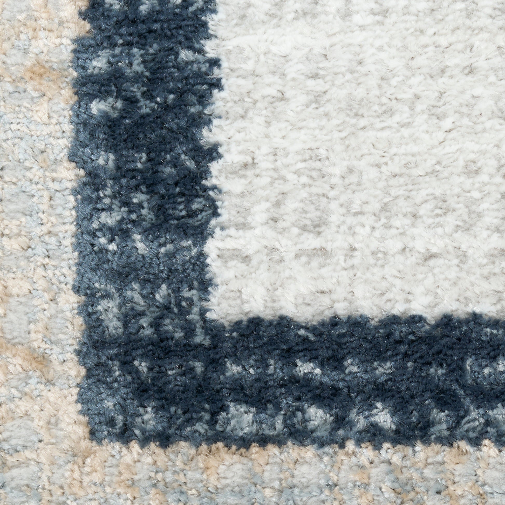 Close-up of a shaggy rug with a navy blue geometric border against cream and beige background.