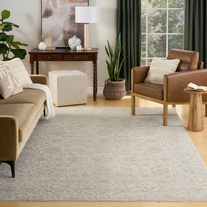 Neutral living room with beige fabric sofa, brown leather armchair, gray patterned rug, wooden console, and greenery.