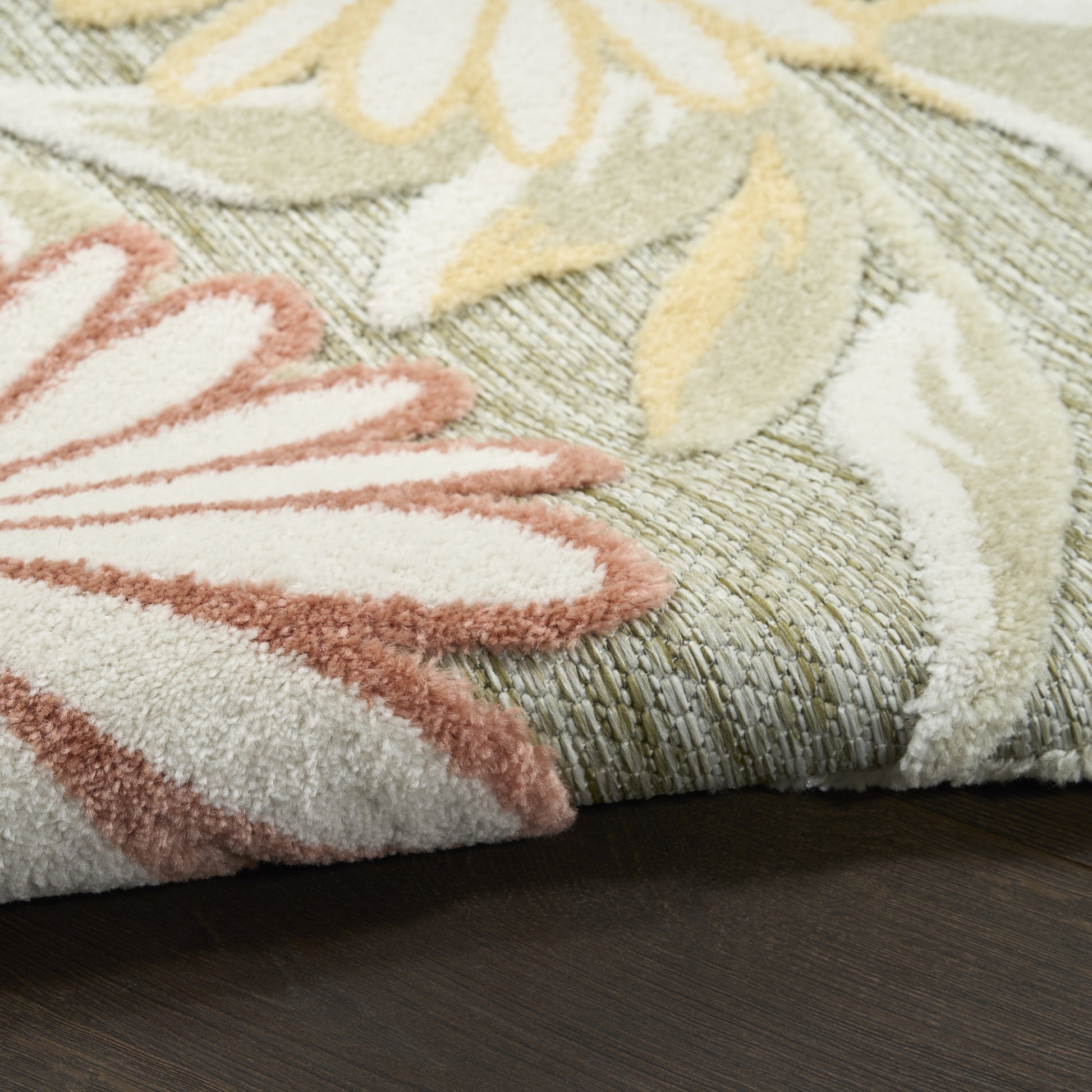 Pastel floral area rug with pink, cream and yellow petals on a green woven base; shaggy pile and folded edge on dark wood.