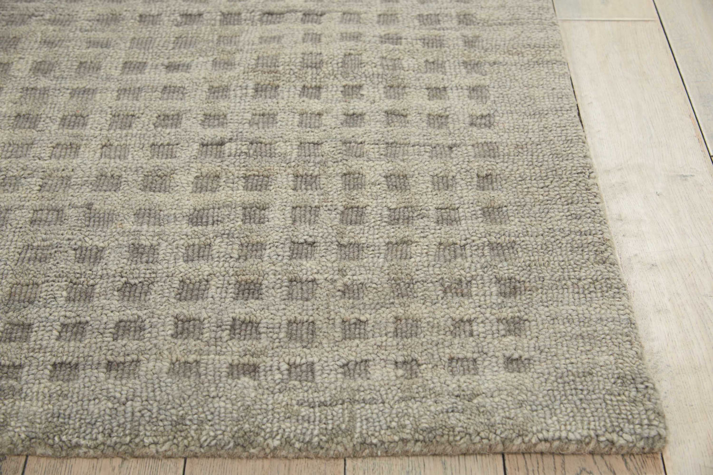 Taupe-gray rug with a subtle square grid pattern and looped texture, resting on light wood flooring.