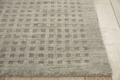 Taupe-gray rug with a subtle square grid pattern and looped texture, resting on light wood flooring.