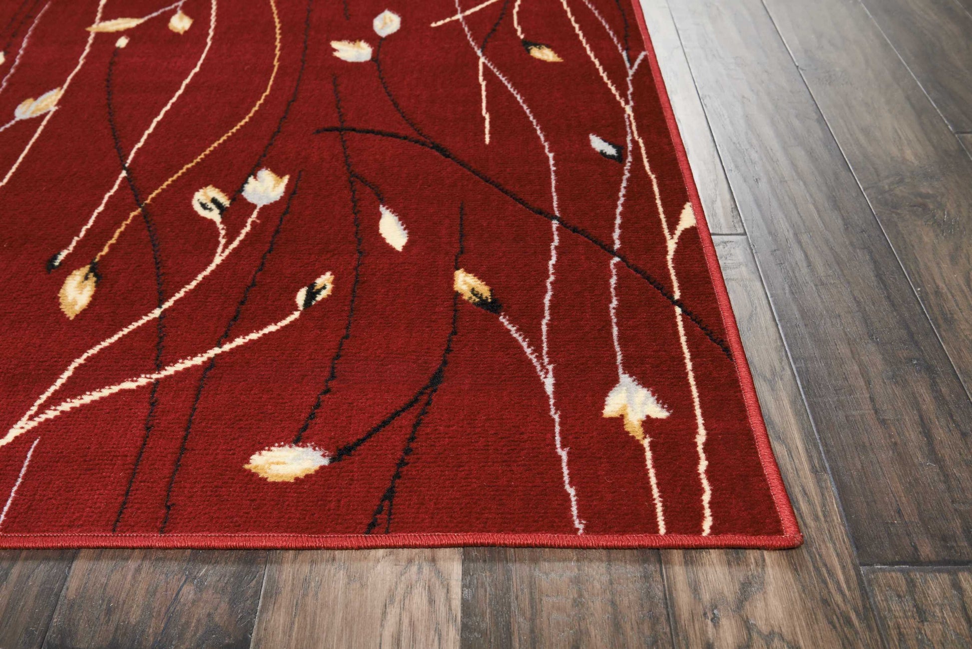 Red area rug with abstract twig pattern in white, black, tan and yellow on a wood floor.