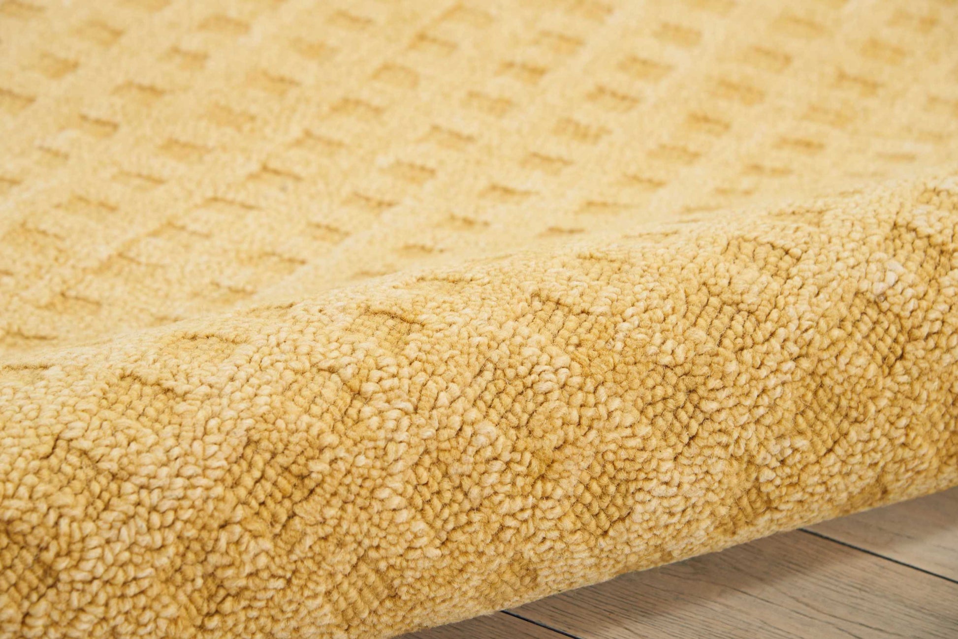 Golden beige shag rug with thick, plush pile and subtle geometric pattern, rolled edge on wood floor.