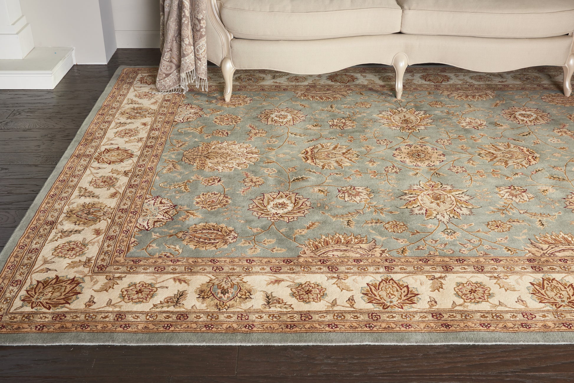 Traditional oriental area rug with a blue central field, ivory/beige border and floral motifs in a living room.