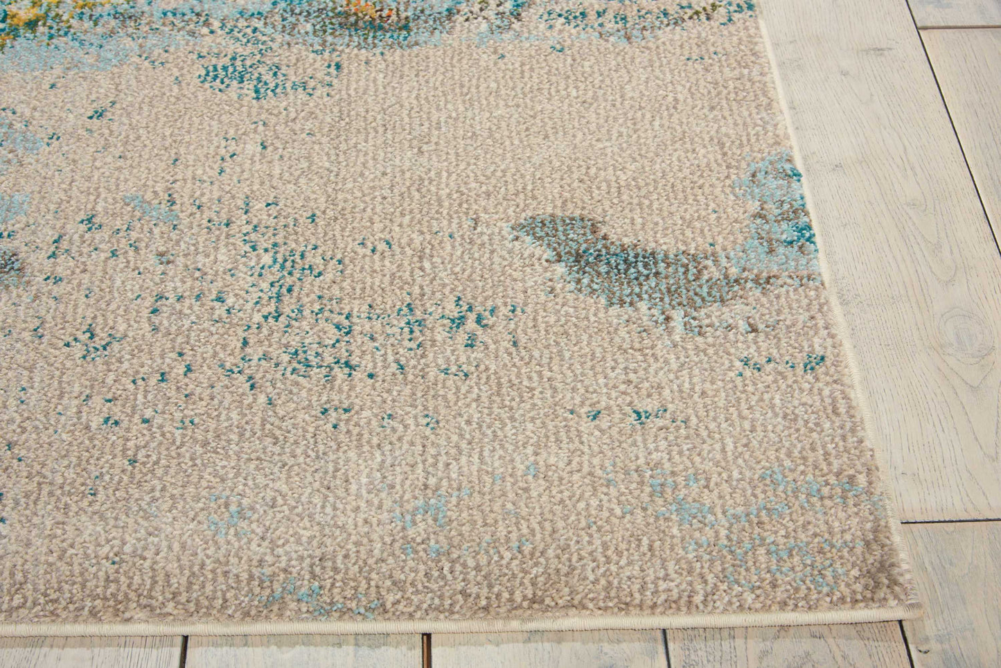 Rectangular beige woven area rug with teal blue distressed pattern on light wooden floor.