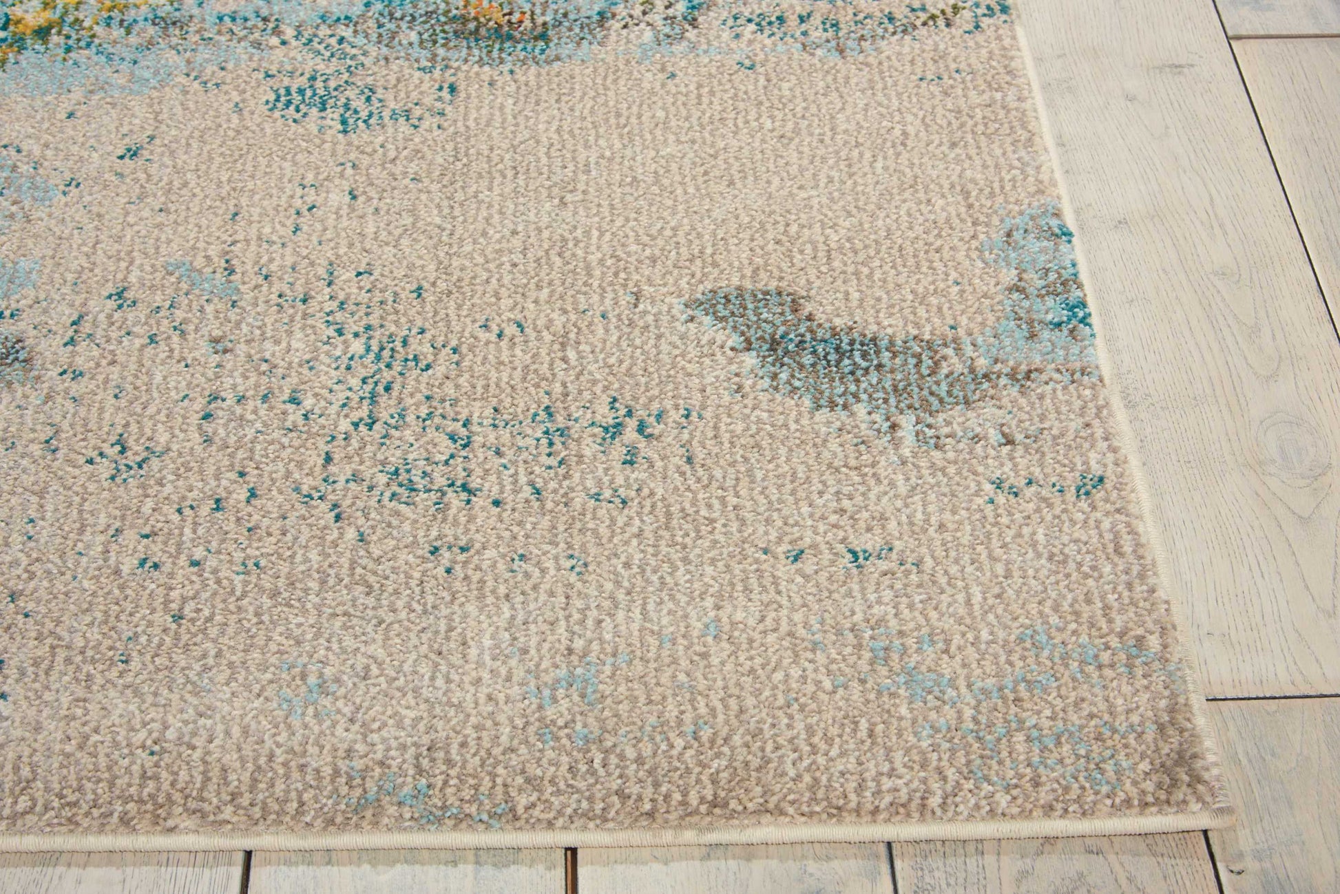 Rectangular beige woven area rug with teal blue distressed pattern on light wooden floor.