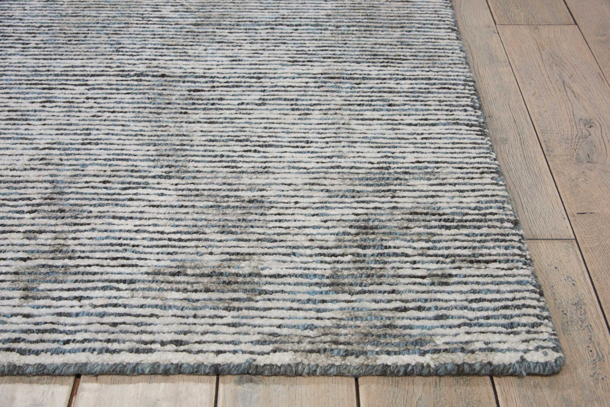 Blue-gray striped rug with low pile texture on wood floor