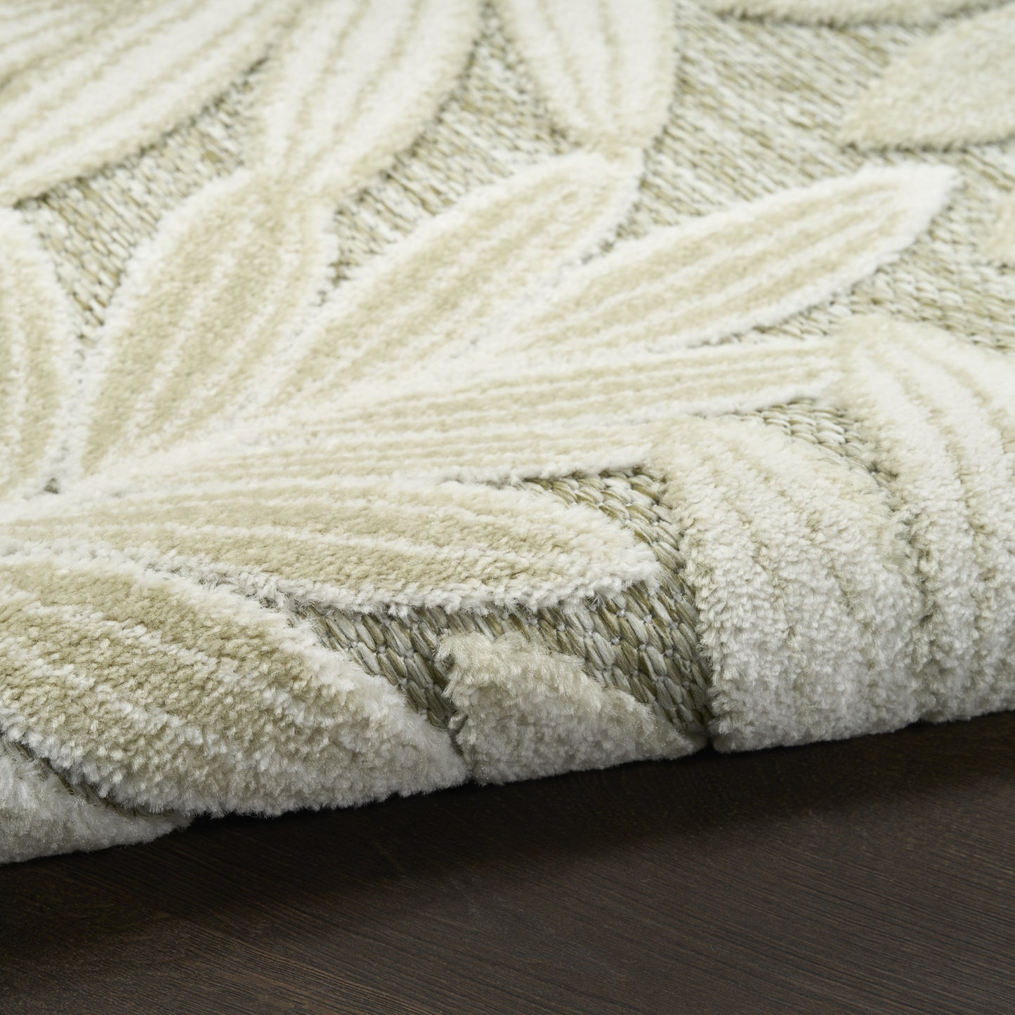Cream textured rug with woven leaf pattern and plush pile on dark wood floor.