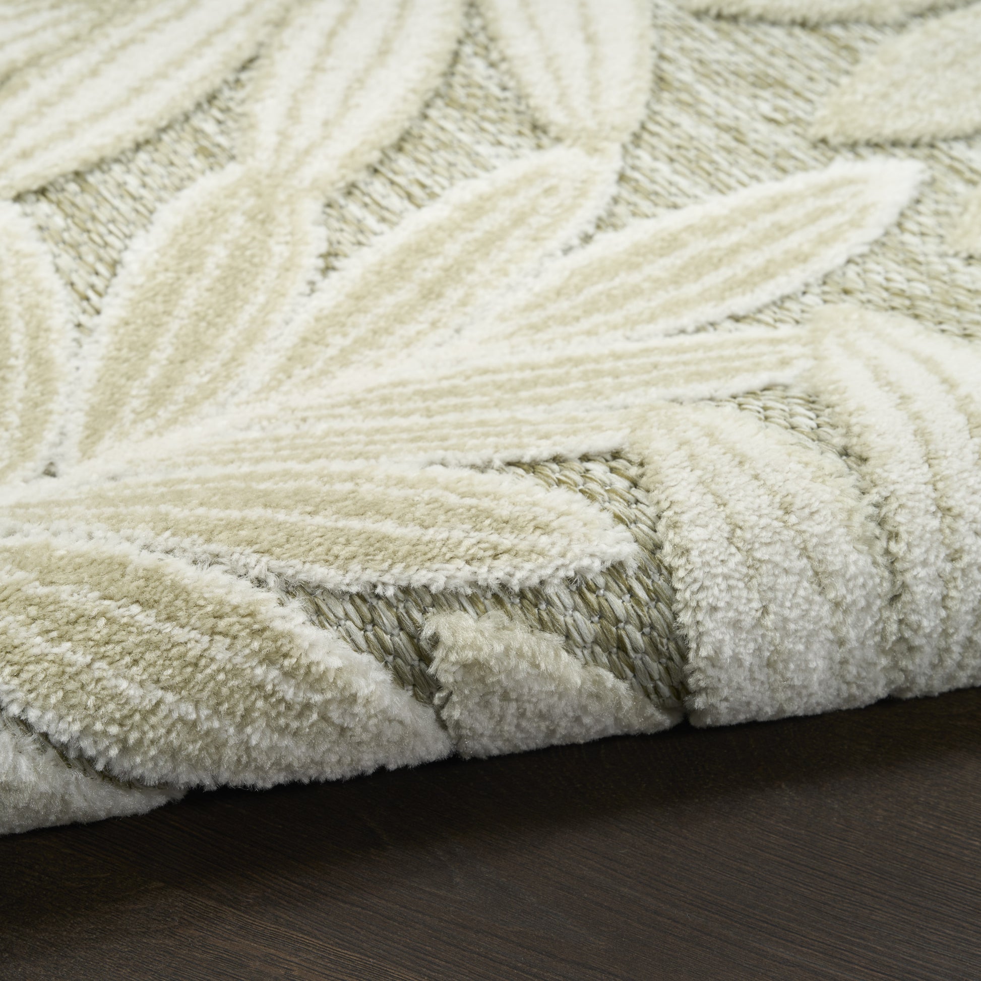 Cream textured rug with woven leaf pattern and plush pile on dark wood floor.