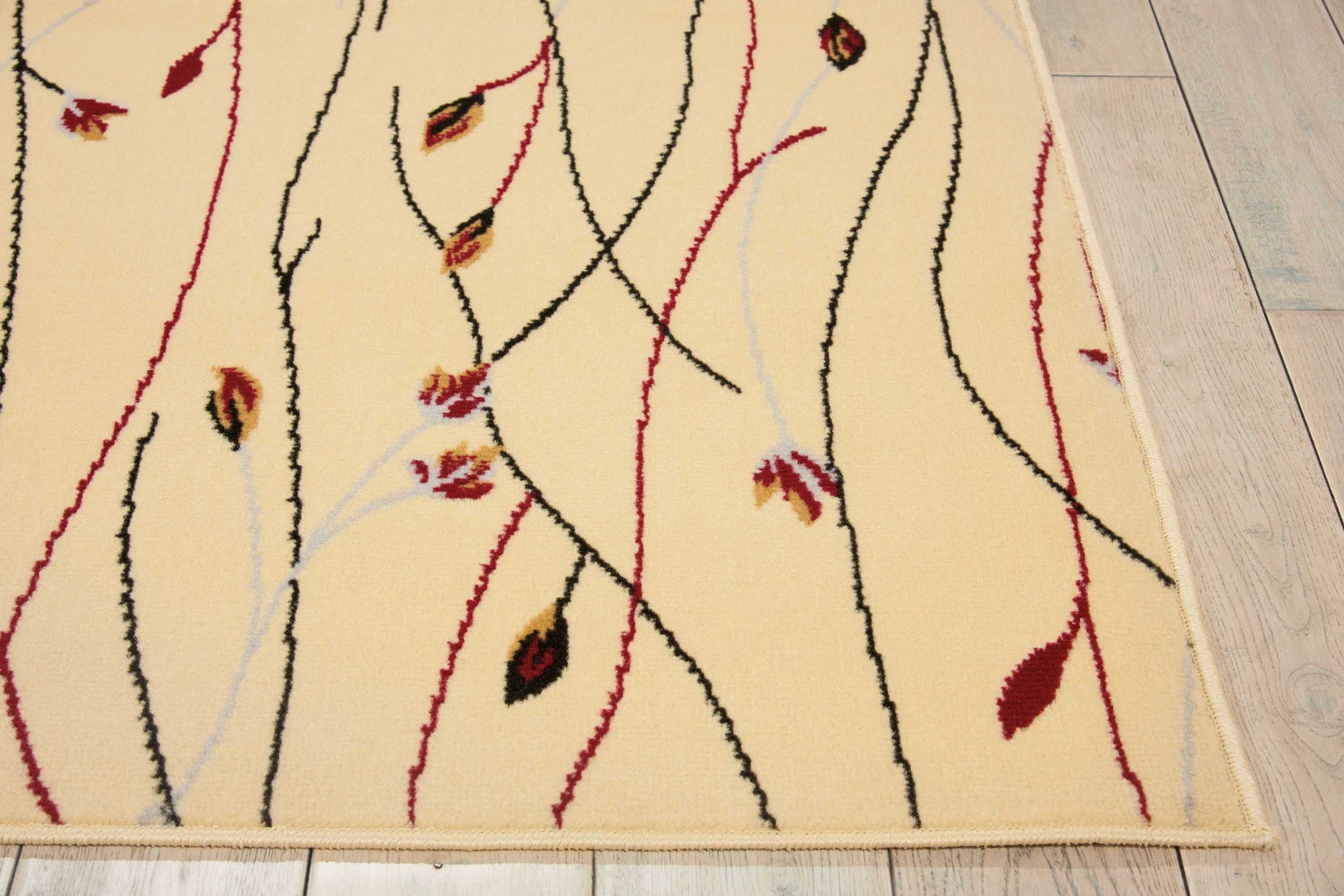 Beige area rug with abstract black and red curving lines, pale blue accents and leaf motifs; tan border on light wood floor.