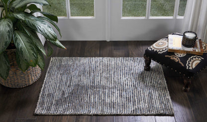 Grey striped low-pile area rug on dark wood floor with potted plant and ornate black-and-gold coffee table near glass doors.
