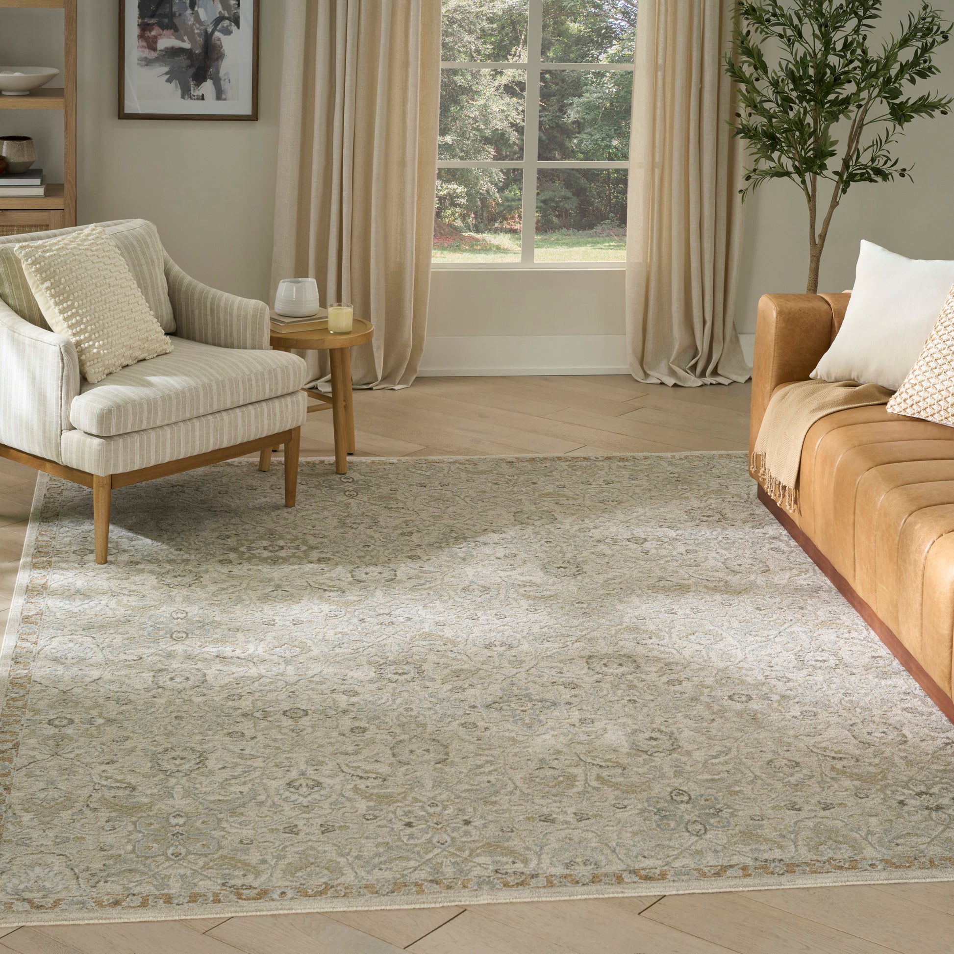 Cozy living room with a vintage beige area rug, cream armchair, tan sofa, wooden side table, & potted plant by a window
