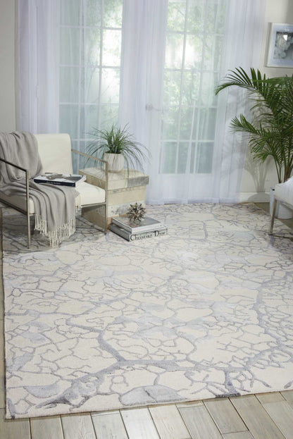 Contemporary living room with a cracked-stone rug, cream metal-framed armchair, gray throw, and potted plants.