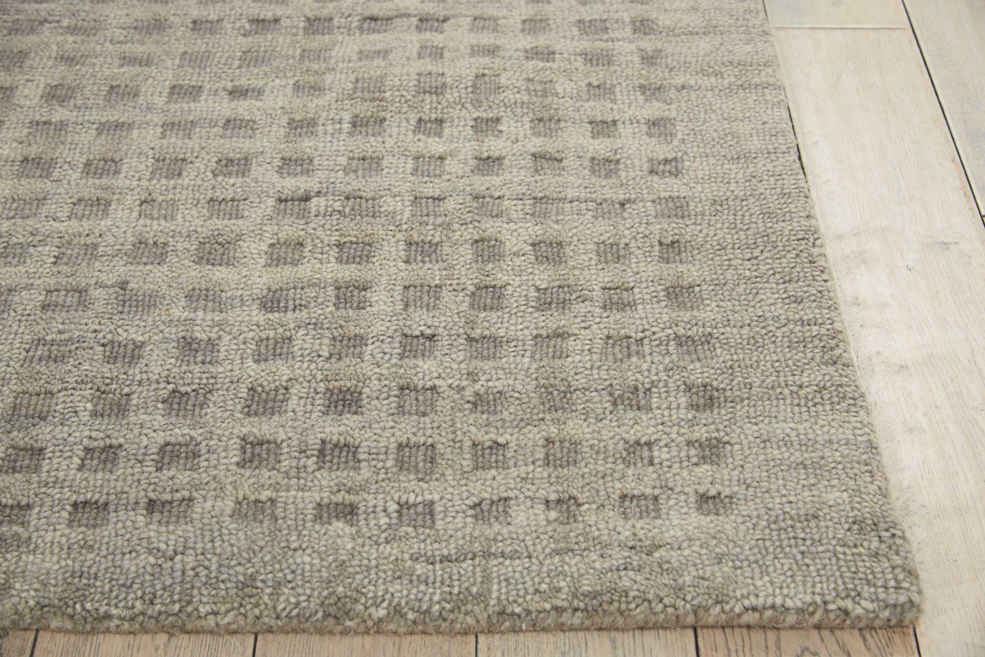 Neutral beige-gray rug with a subtle square grid pattern and thick pile, laid on light wood flooring.