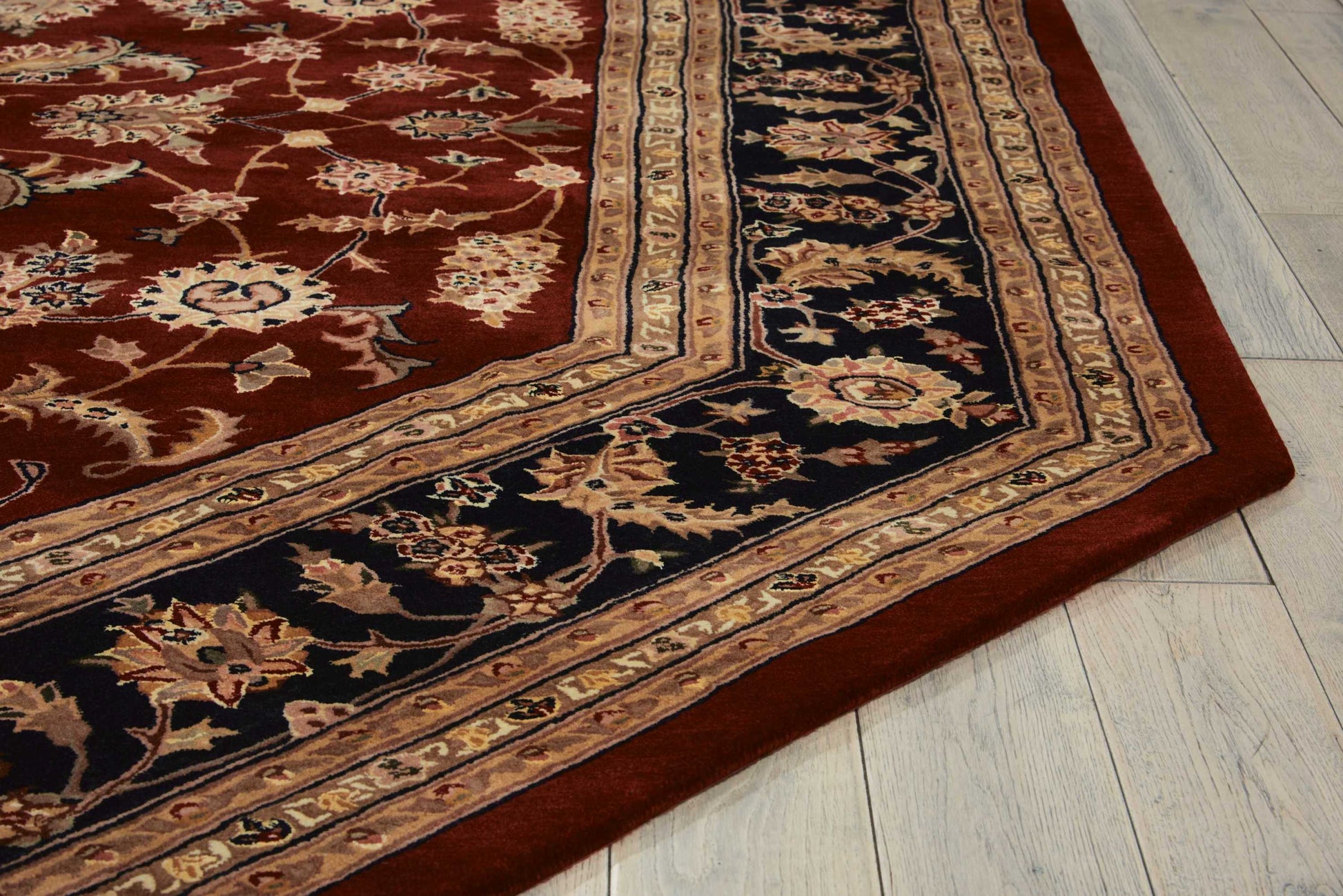 Traditional Persian-style rug with red field, navy and beige borders and gold floral motifs on light wood floor.