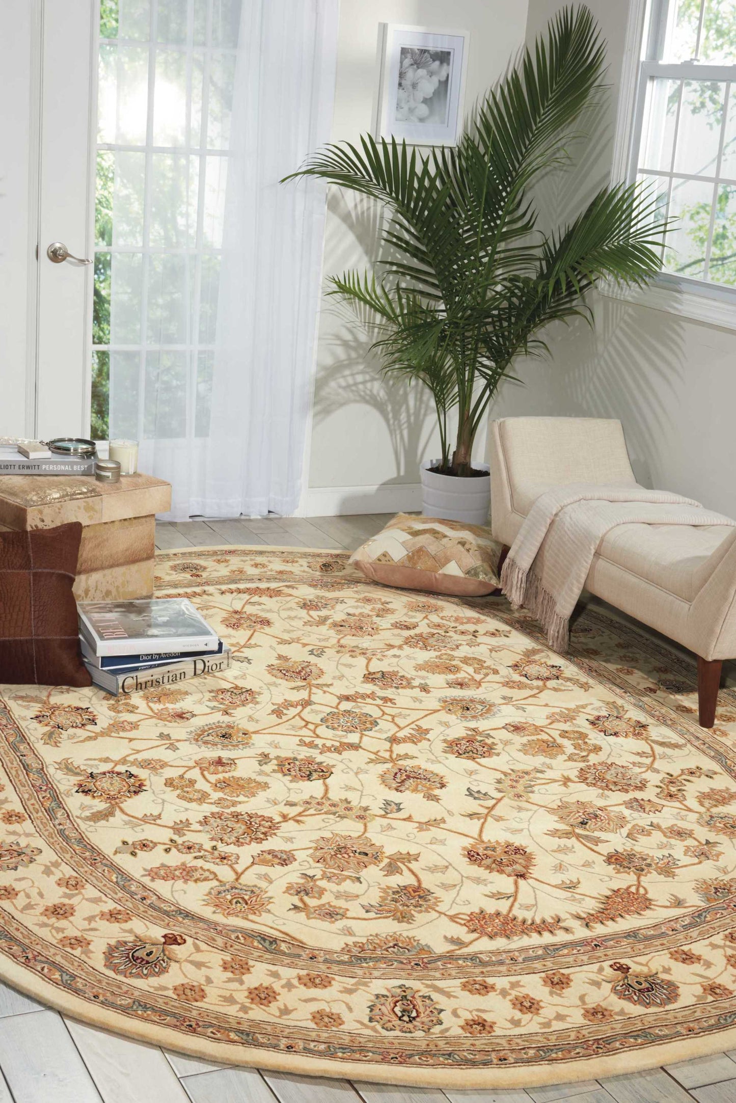 Beige ornate area rug with brown floral motifs in a sunny living room; beige chaise, coffee table, and tall potted palm.