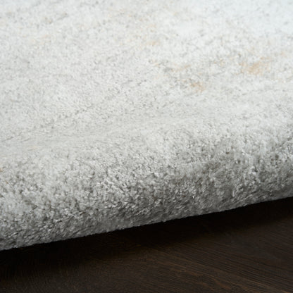 Close-up of light gray plush shag rug with dense pile on dark wood floor.