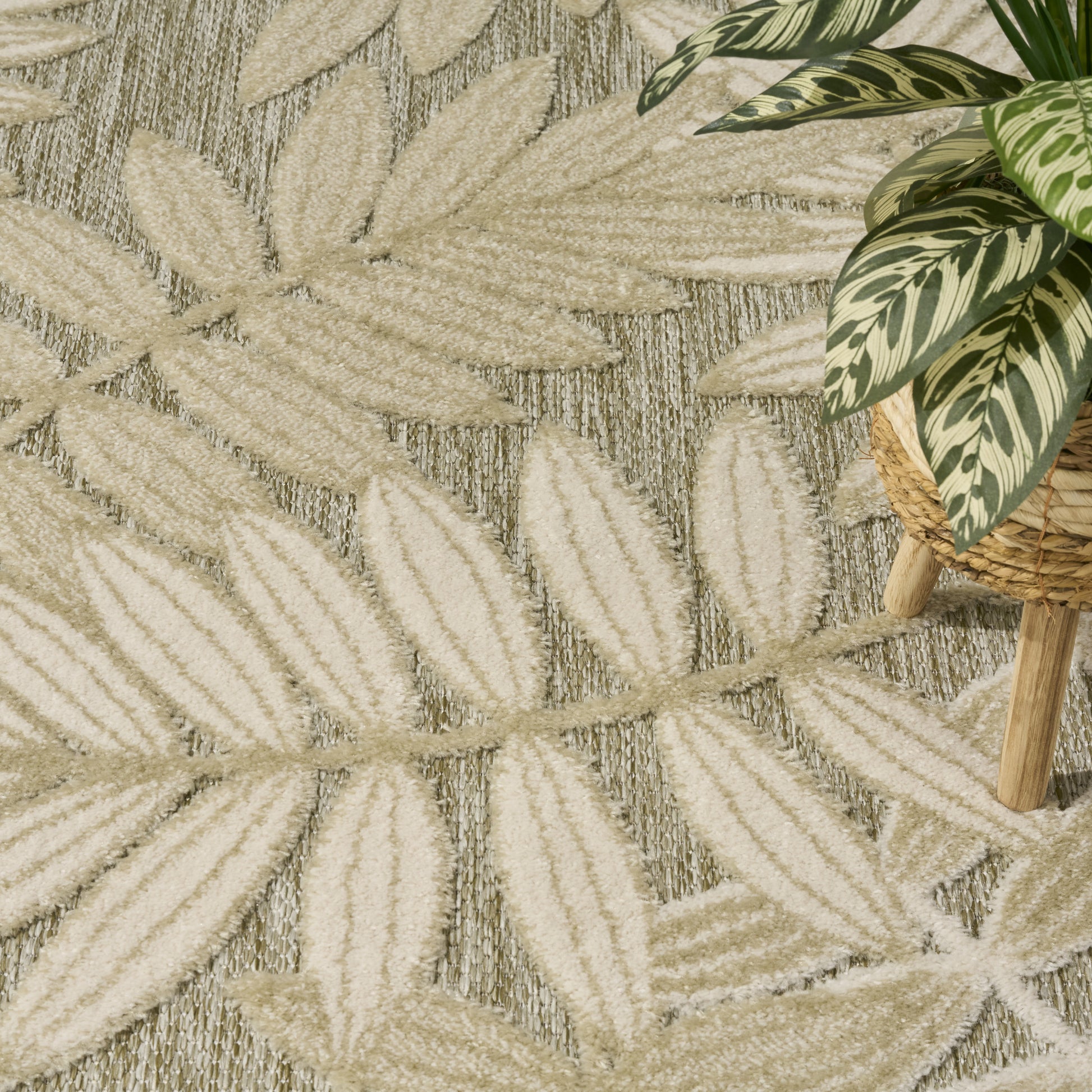 Beige leaf-pattern rug in natural fibers with raised palm leaf motifs, paired with a variegated plant in a woven basket.