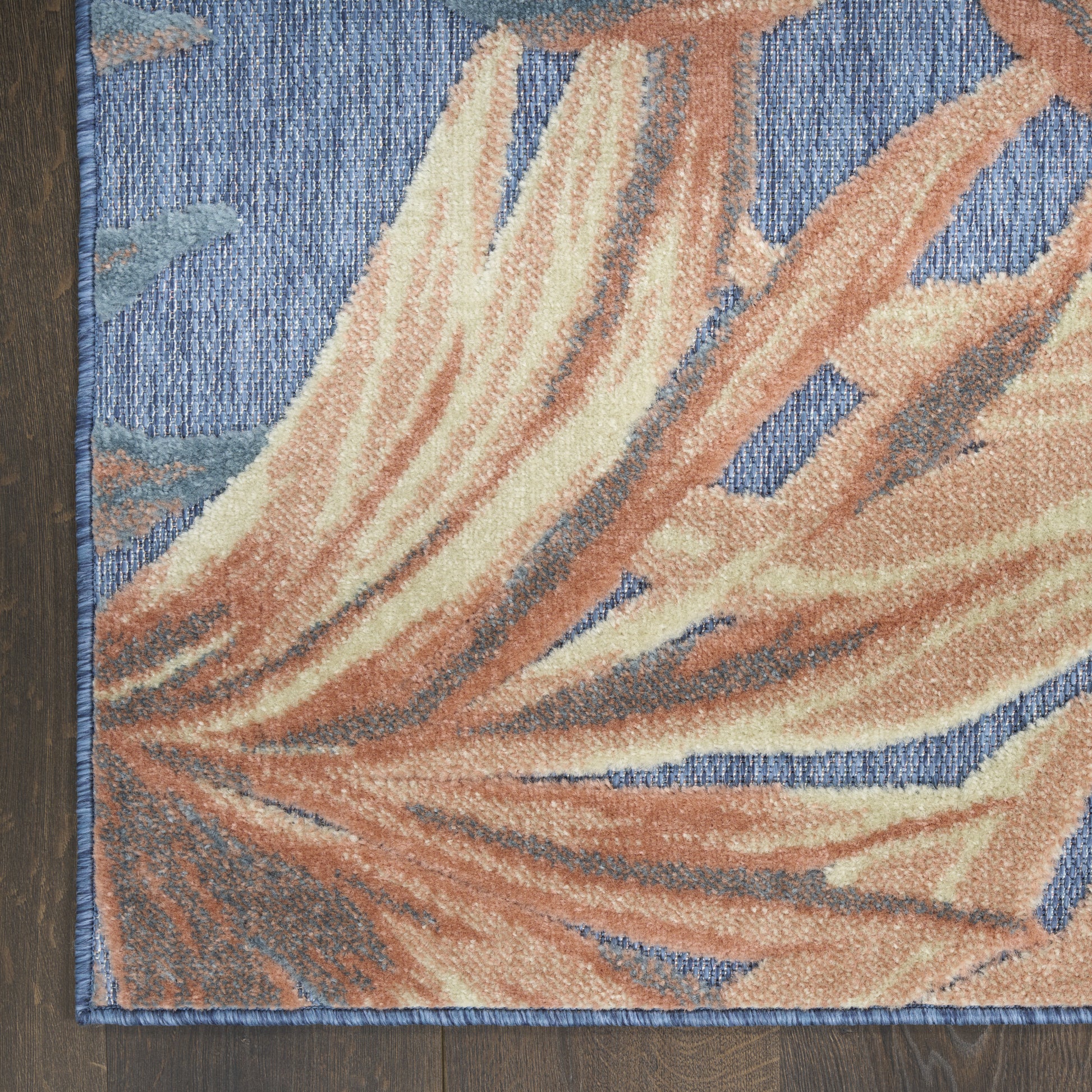 Textured area rug with blue background and peach-orange palm leaf pattern, blue edge trim on dark wood floor.