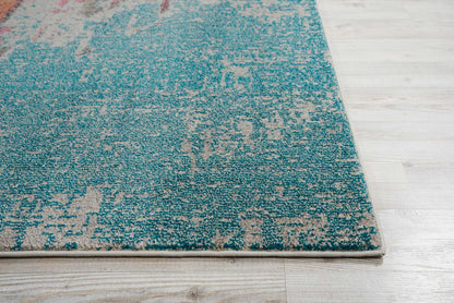 Teal blue distressed area rug with beige abstract pattern, bound edge, placed on light wooden floor.