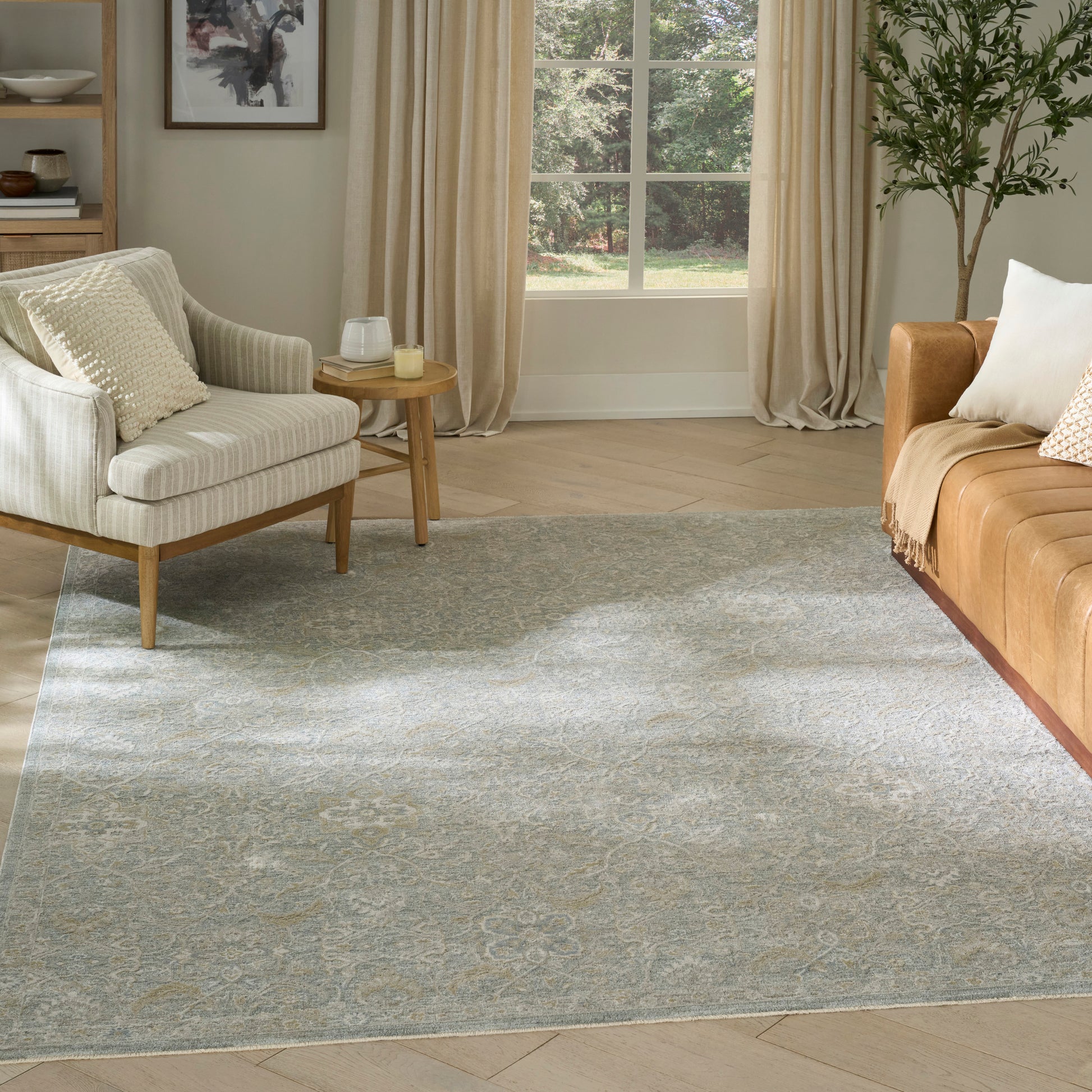 Living room with light gray patterned rug, beige striped armchair, round wooden side table, tan leather sofa, cream pillows.