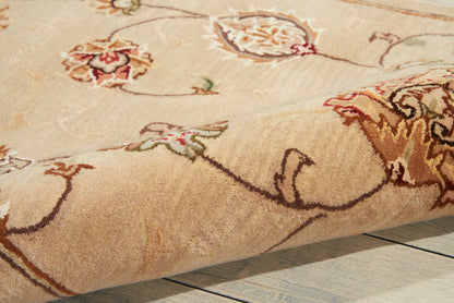 Beige ornate floral area rug with brown and red accents, plush pile, edge folded on pale wood floor.