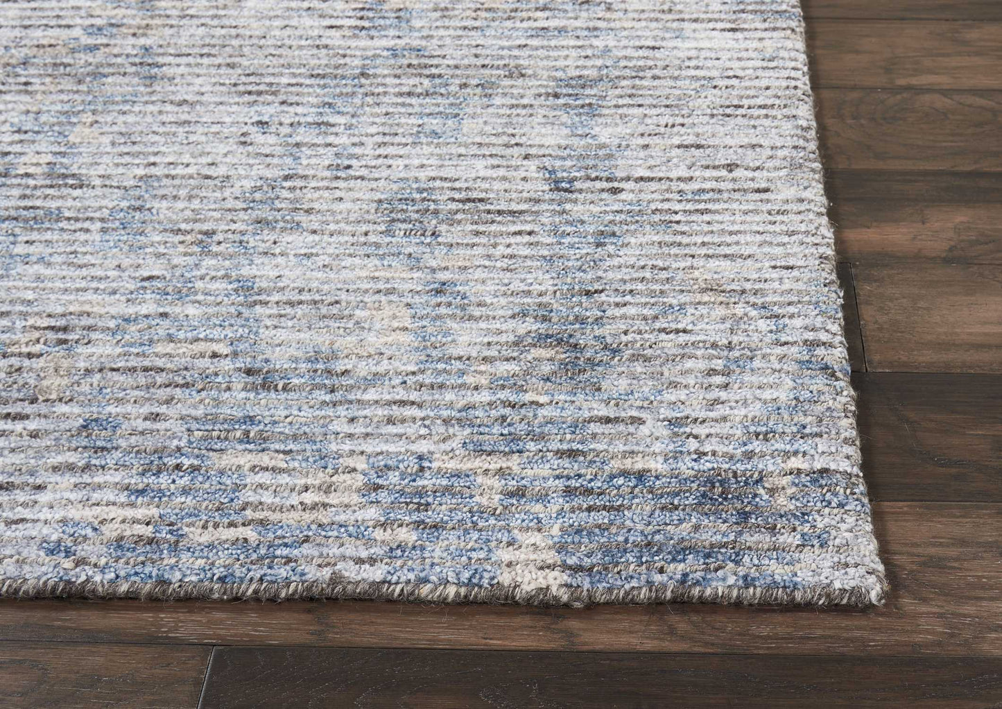 Rectangular area rug in blue and beige with a textured distressed pattern on dark wood floor.