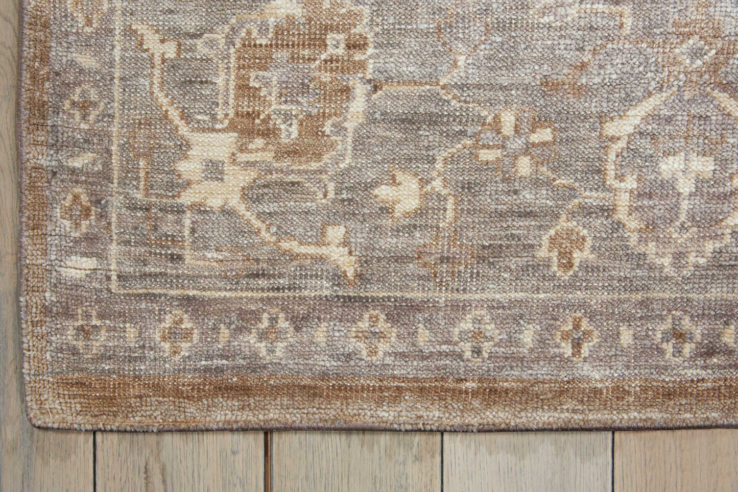 Distressed beige-gray rug with floral border on a wooden floor.
