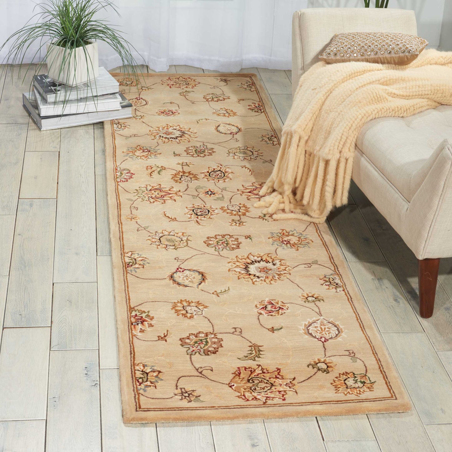 Beige floral runner rug with ornate red and green flowers, tan border, laid along a light wood floor by a beige sofa.