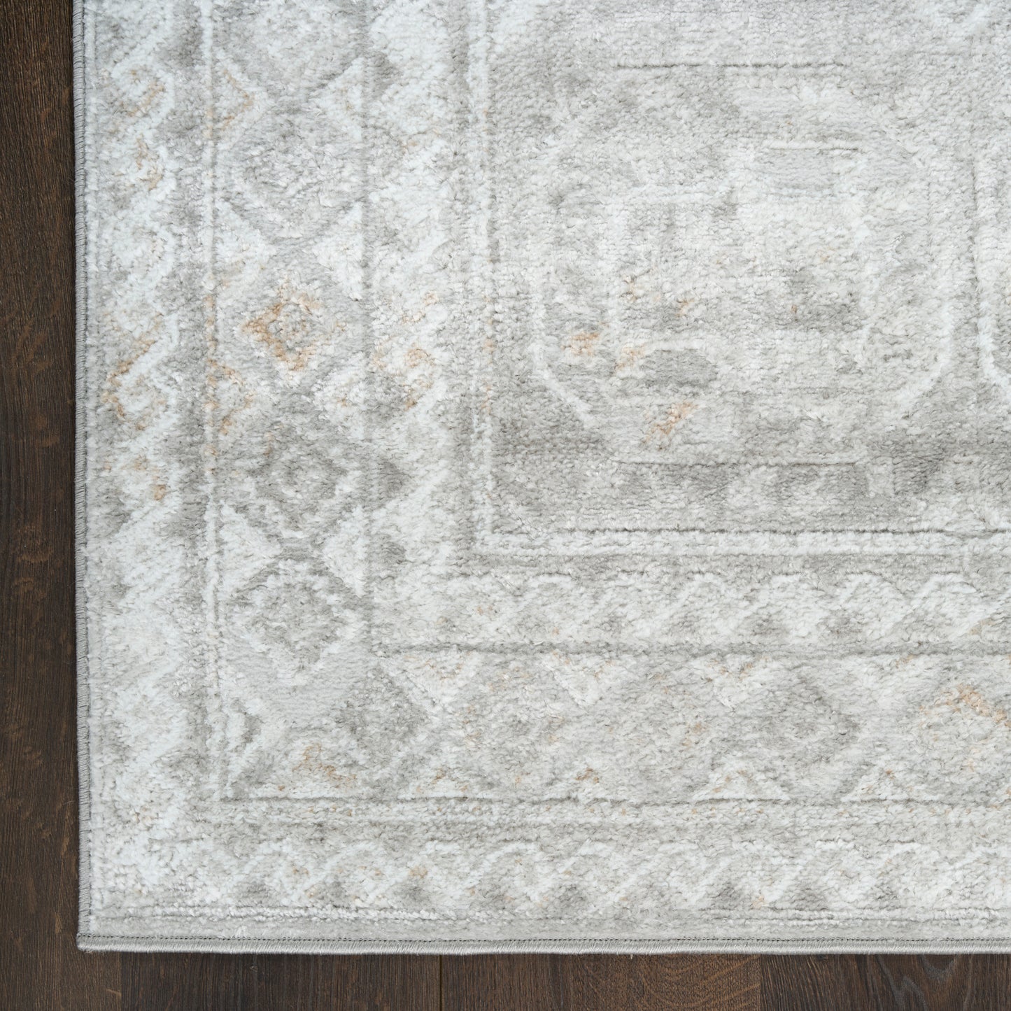 Light gray area rug with subtle geometric border and diamond motifs, beige accents, on dark wood floor.