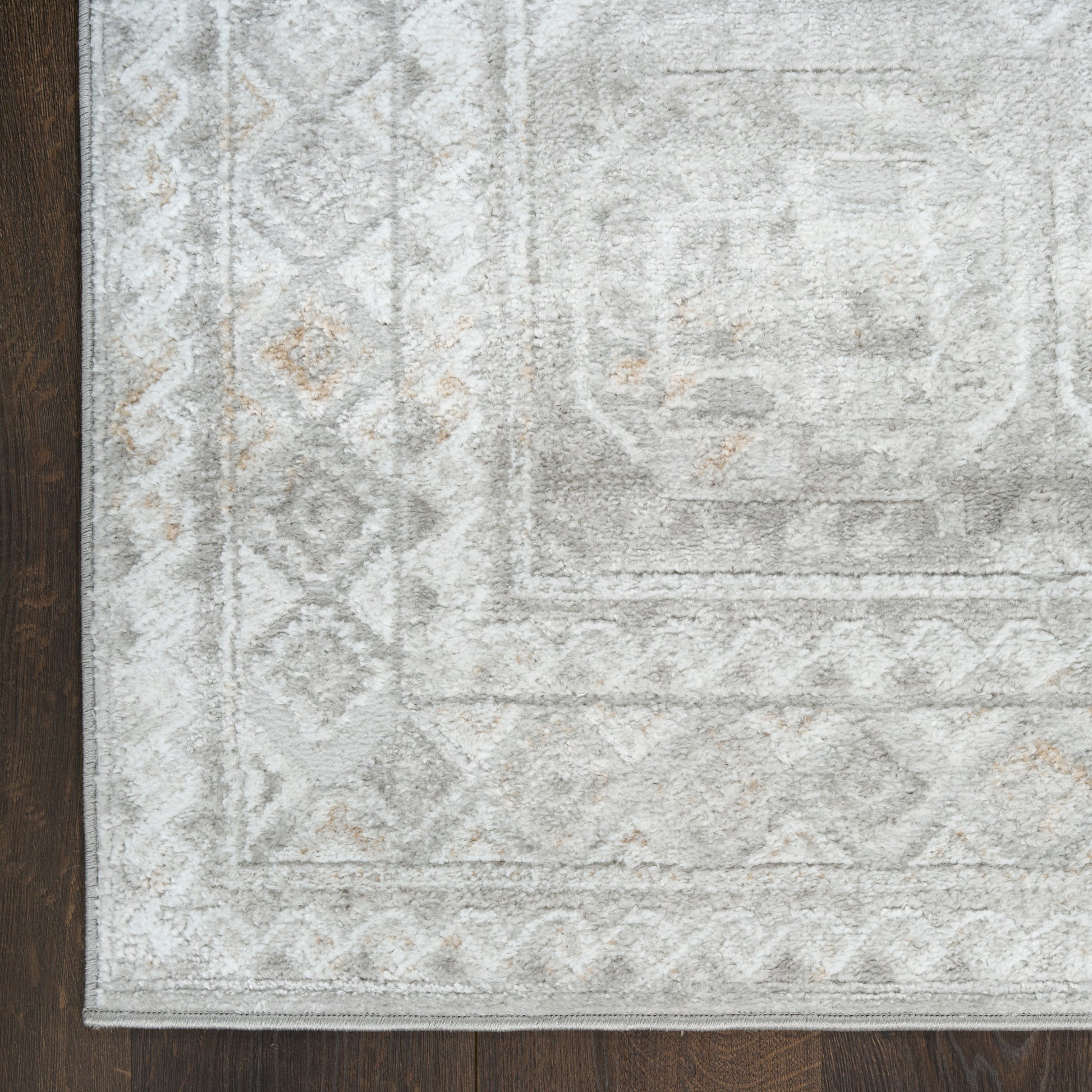 Light gray area rug with subtle geometric border and diamond motifs, beige accents, on dark wood floor.