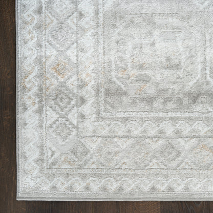 Light gray area rug with subtle geometric border and diamond motifs, beige accents, on dark wood floor.