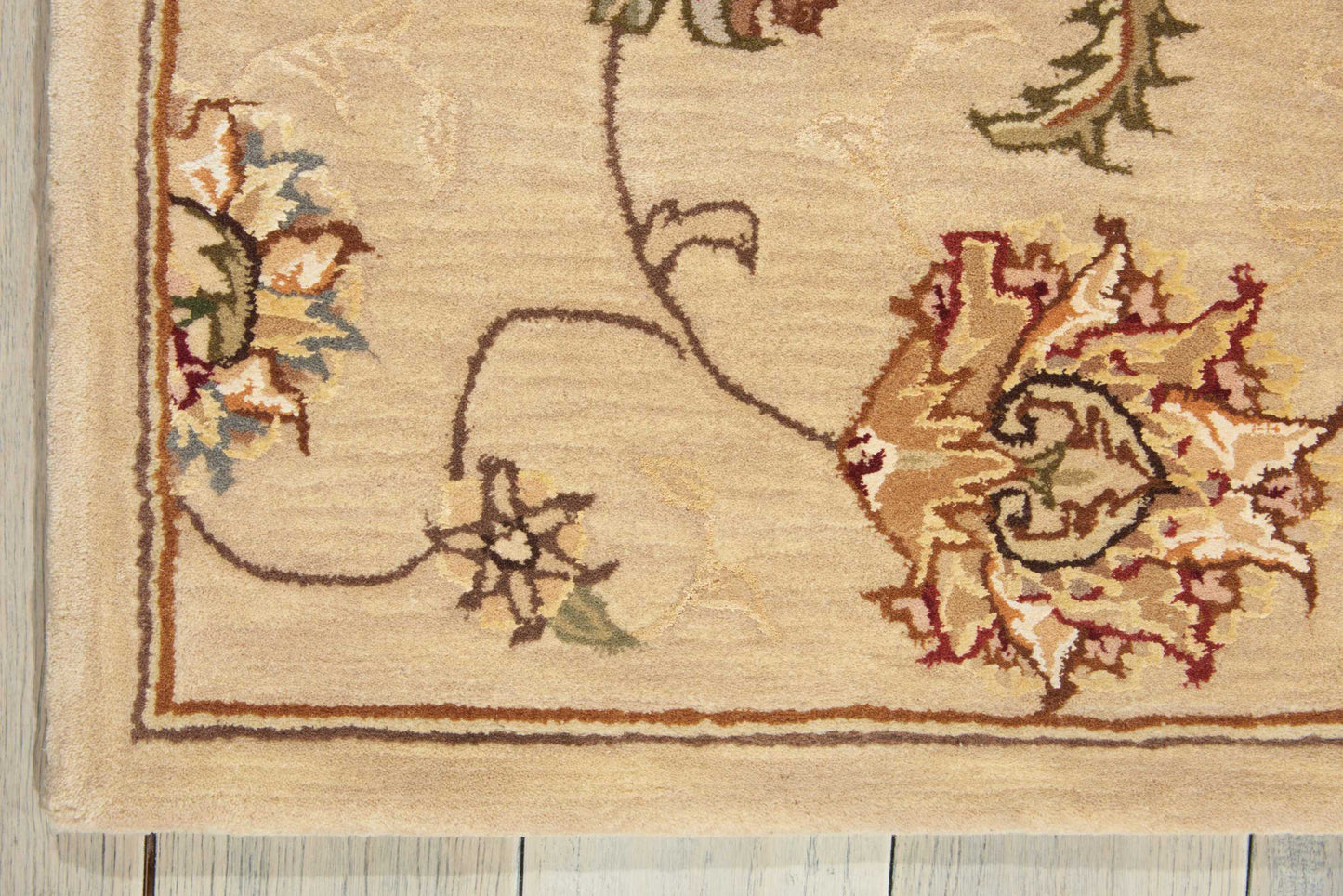 Beige oriental-style woven rug corner with floral vines and border on light wood floor; cream, tan, brown, rust, blue.